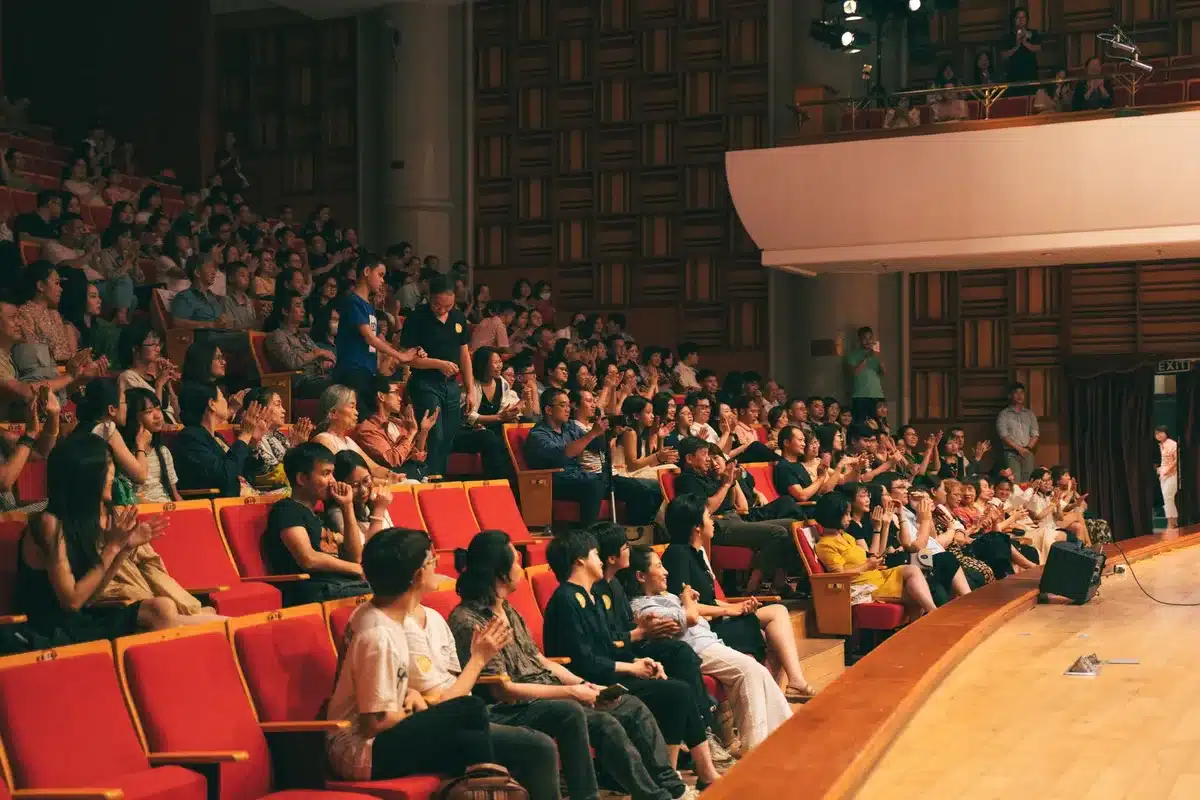 Público entusiasmado aplaudiendo en un teatro durante una presentación.