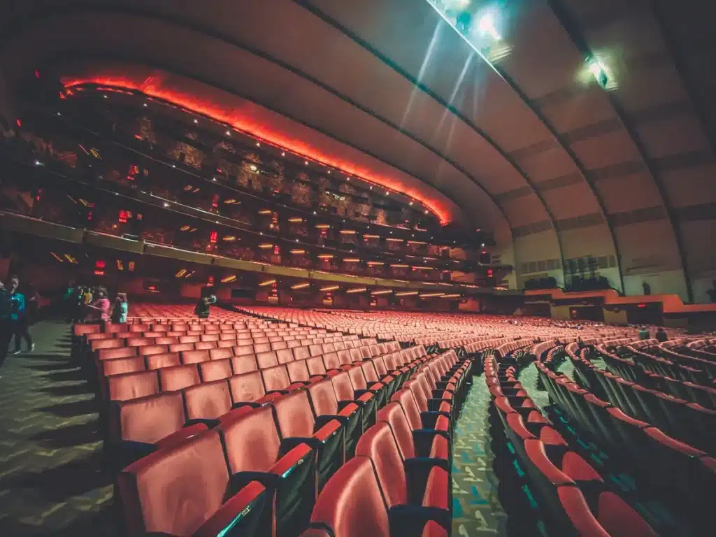 Escena de un escenario de teatro musical con bailarines en silueta bajo luces doradas.