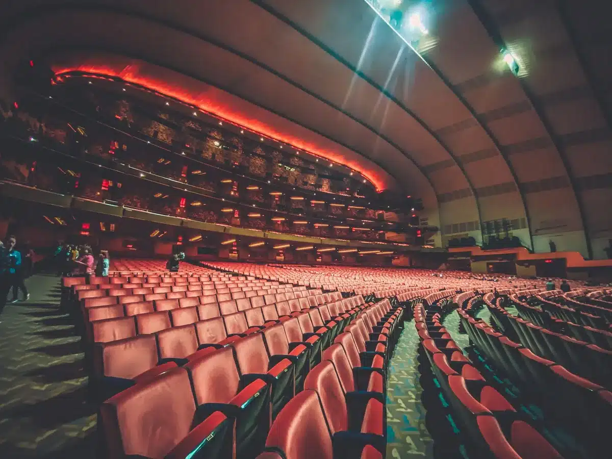 Escena de un escenario de teatro musical con bailarines en silueta bajo luces doradas.