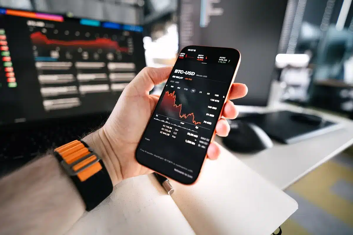 Gráficos financieros con tendencia bajista y símbolos de Bitcoin en una pantalla de trading