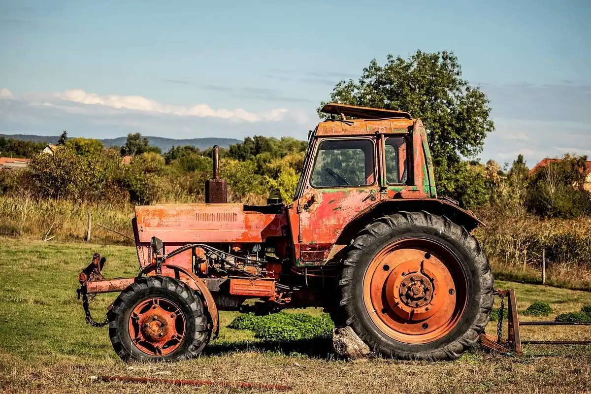 Close-up of anonymous farmers' hands on tractor controls beside stacked cane bundles near a rural road, no faces visible