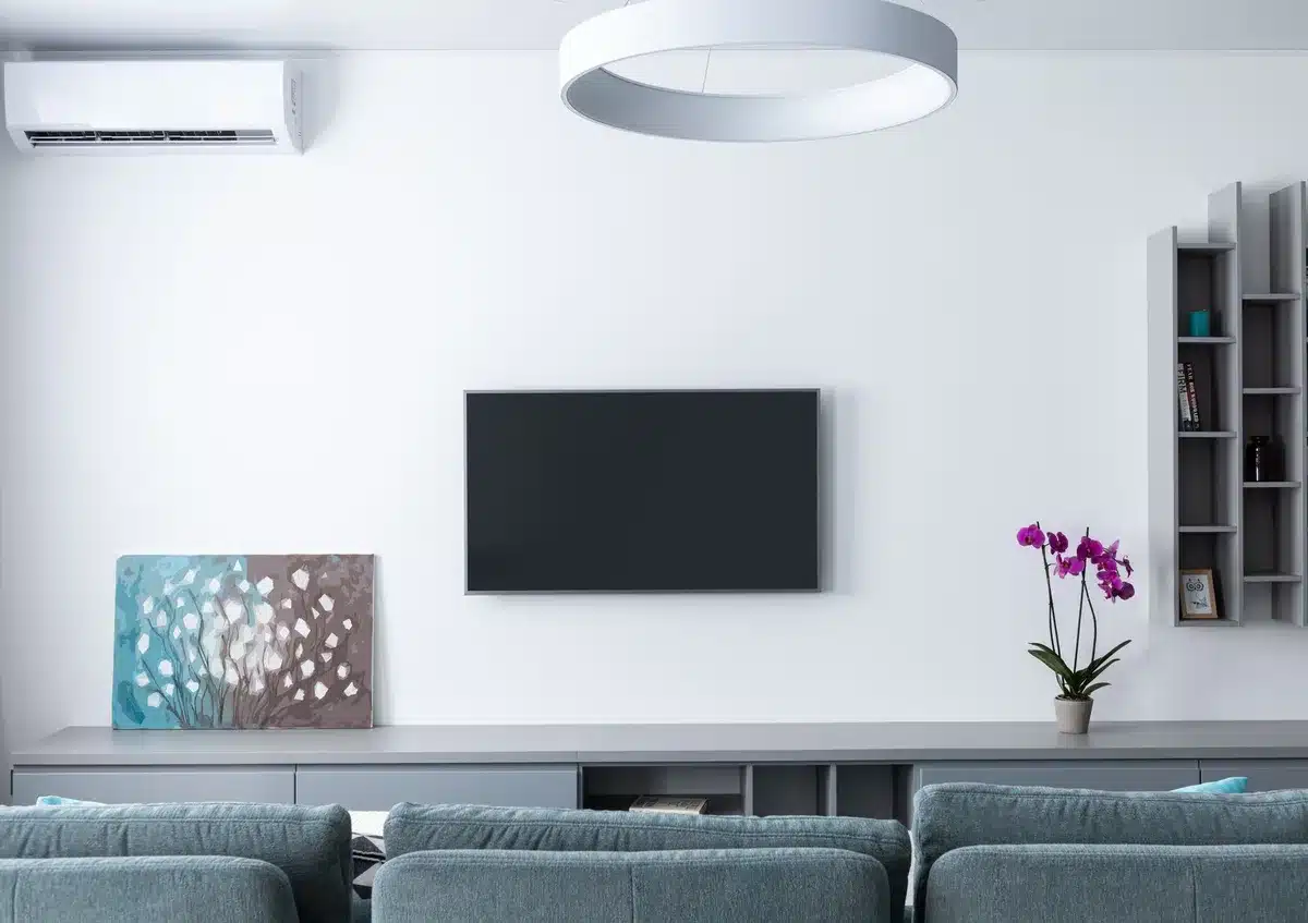 A clean living room scene with a large unbranded TV on a low media console, soft reflections on the screen, a dim lamp and a remote on a coffee table — modern home environment