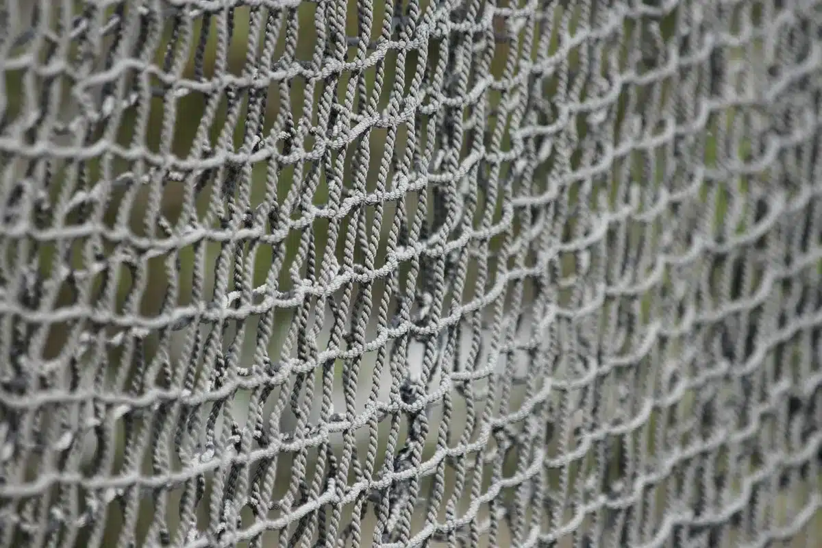 Close-up of an anonymous fisher's worn net with sticky oil residue, blurred industrial vessels in background