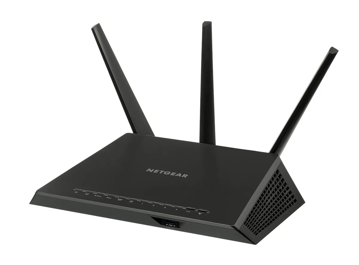 Router on a small table next to a laptop and an open notebook showing a simple spreadsheet of speed test results; no brand visible, home interior, soft daylight