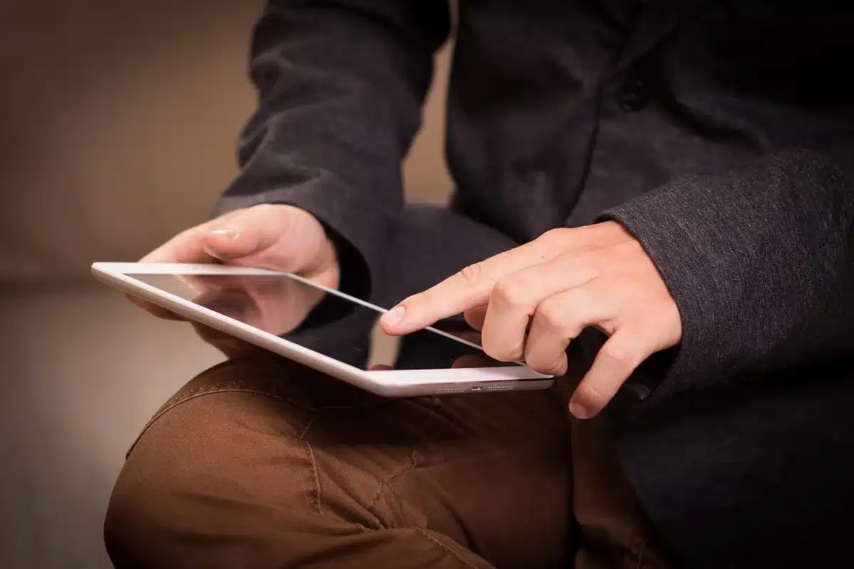 A compact silver tablet resting on a child’s backpack on a wooden table, no logos visible, screen off, small headphones beside it
