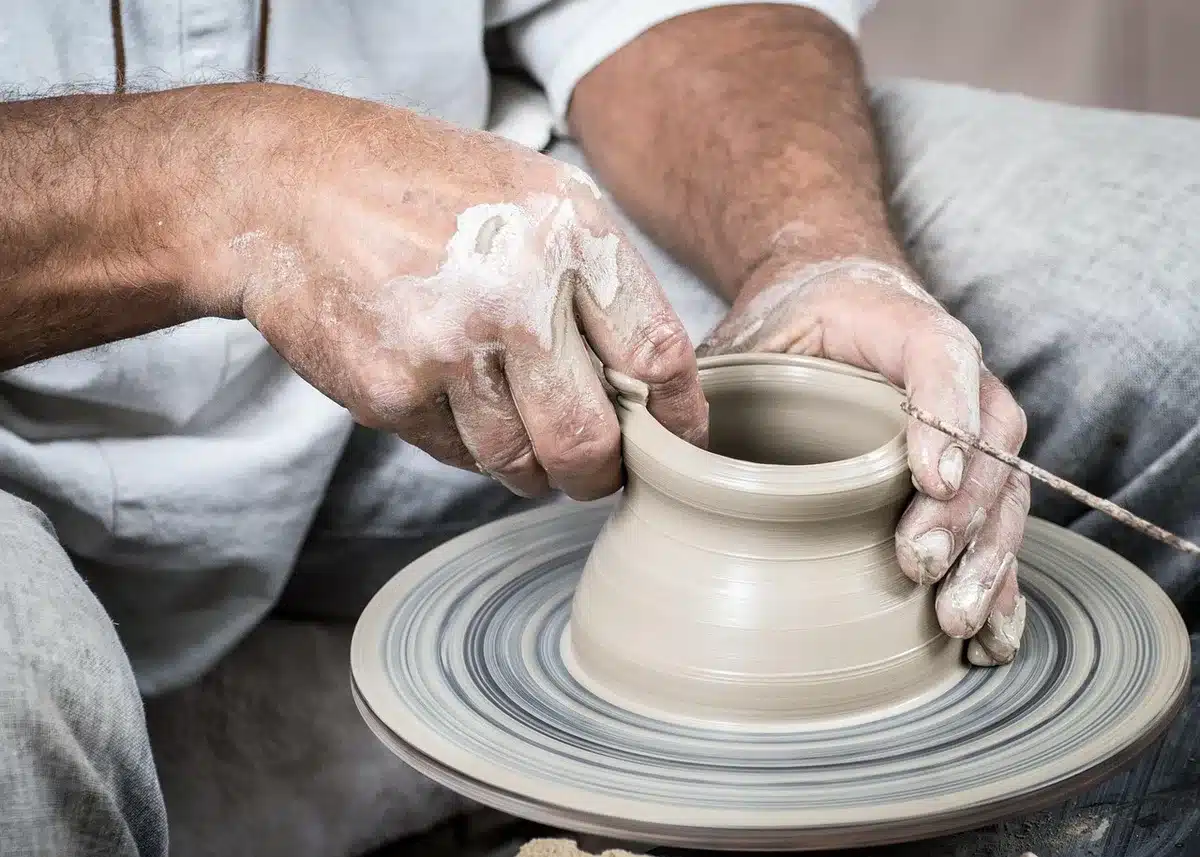 Close-up of anonymous hands shaping clay on a potter's wheel, finished pieces lined behind under soft indoor lighting